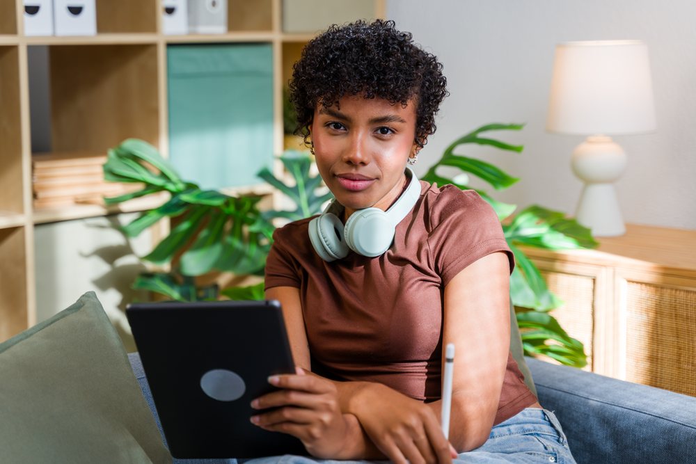 Woman with headphones on couch using tablet and stylus in living room, Spain.