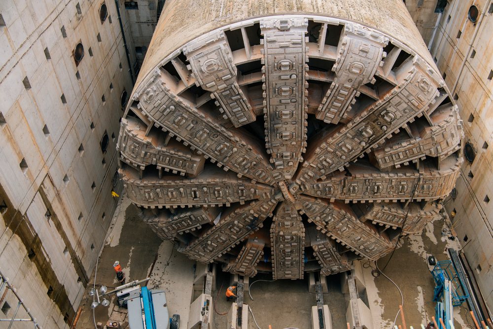 A large tunnel boring machine is positioned inside a concrete construction site with workers nearby, the tunnel boring machine, drilling, USA.
