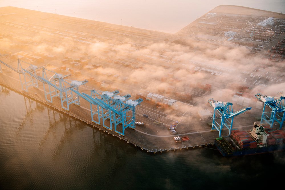 Container terminal with shipping cranes and cargo ship at the Port of Long Beach, partially covered in fog during sunset, CA, USA.