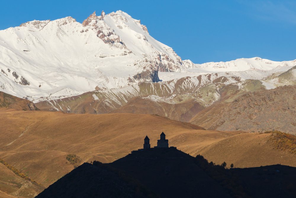 Silhouette of Gergeti Trinity Church on a hill at Sunrise with snow-capped mountains in the background, Georgia.