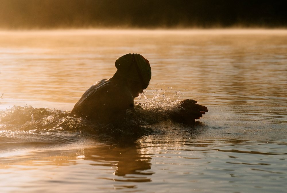 Swimmer performing a stroke in calm lake water at early morning with sunlight reflecting, USA.