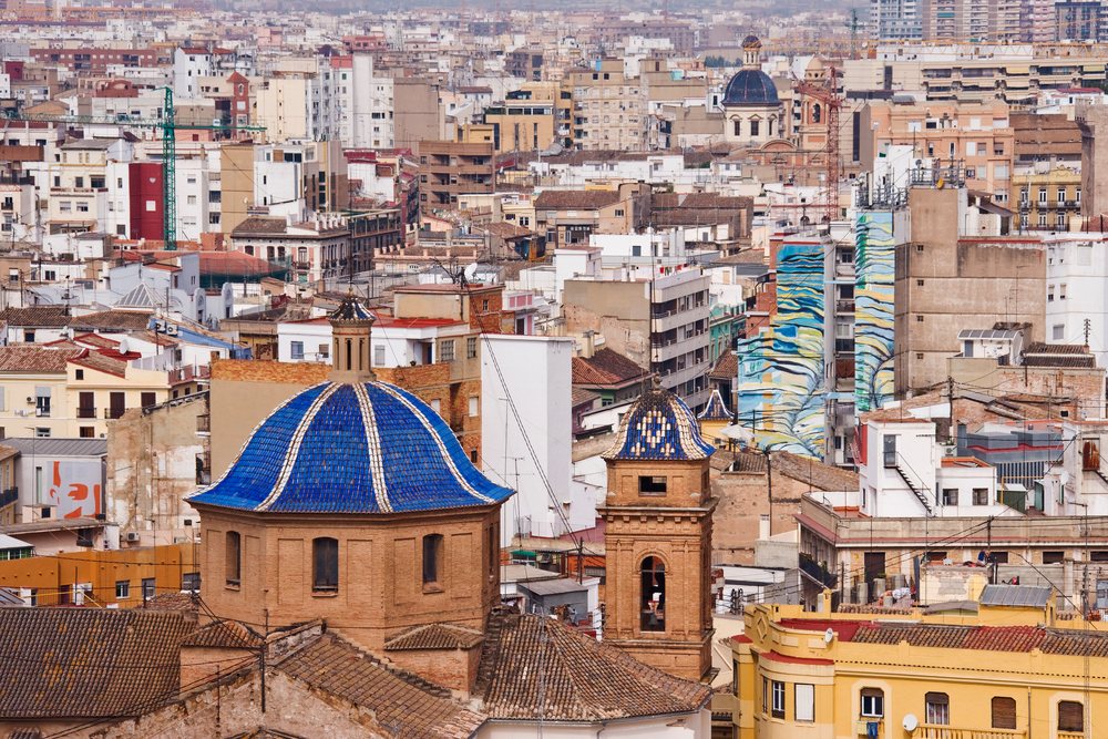 Cityscape of Valencia, showing densely packed buildings with varied rooftops and a blue-domed church tower, Spain.