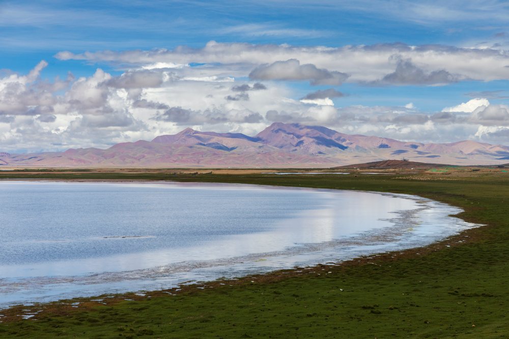 Lake with grassy shore and mountains in Kham Tibet landscape, Amdo County, Autonomous Region of Tibet.