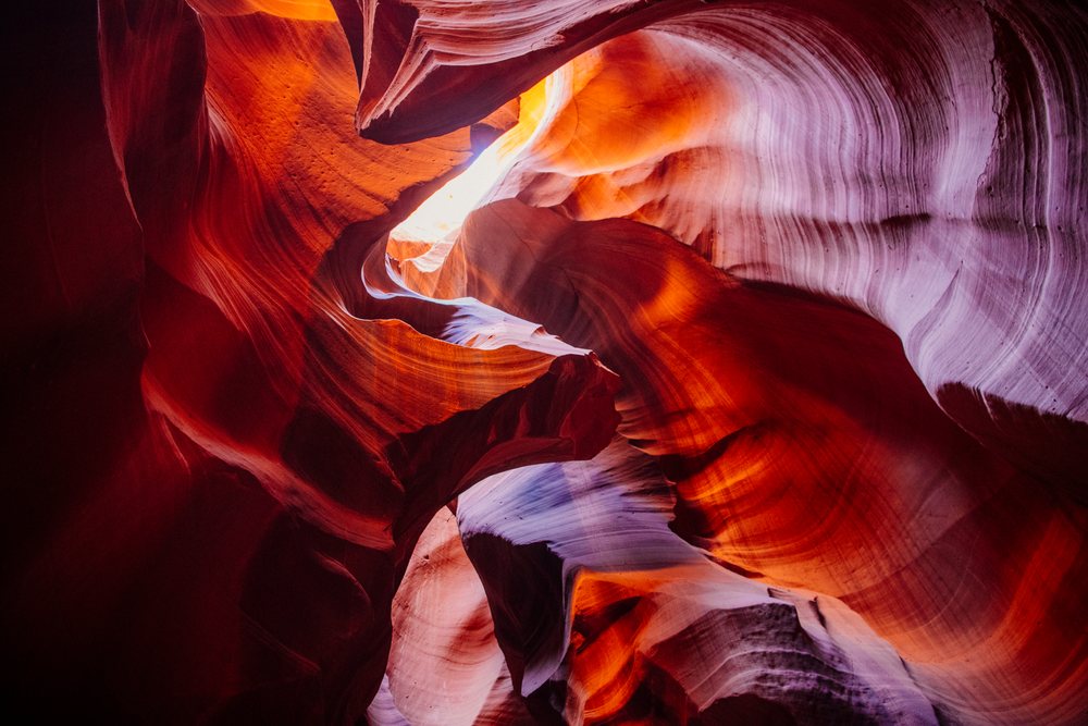 Sunlit curved sandstone rock formations and vibrant orange and purple strata form Antelope Canyon's slot canyon, Navajo Land, Arizona, USA.