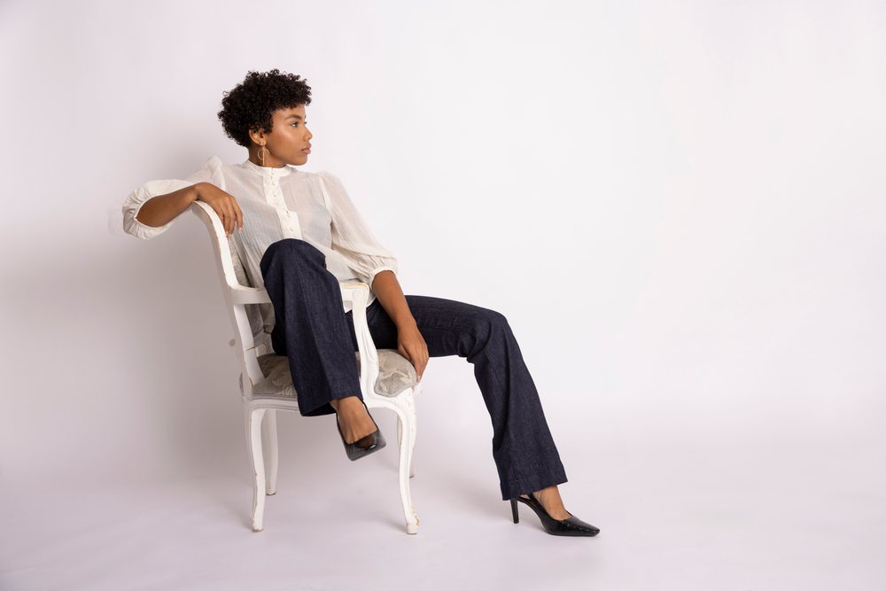 Woman sitting on white chair wearing white blouse and dark pants, fashion, young culture.