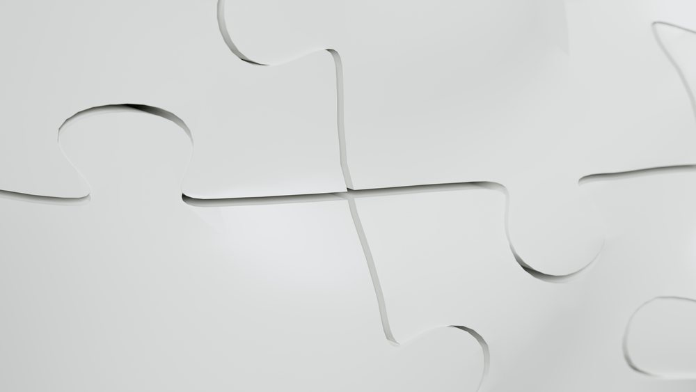 Closeup of white interlocking jigsaw puzzle pieces fitting together on a smooth surface.