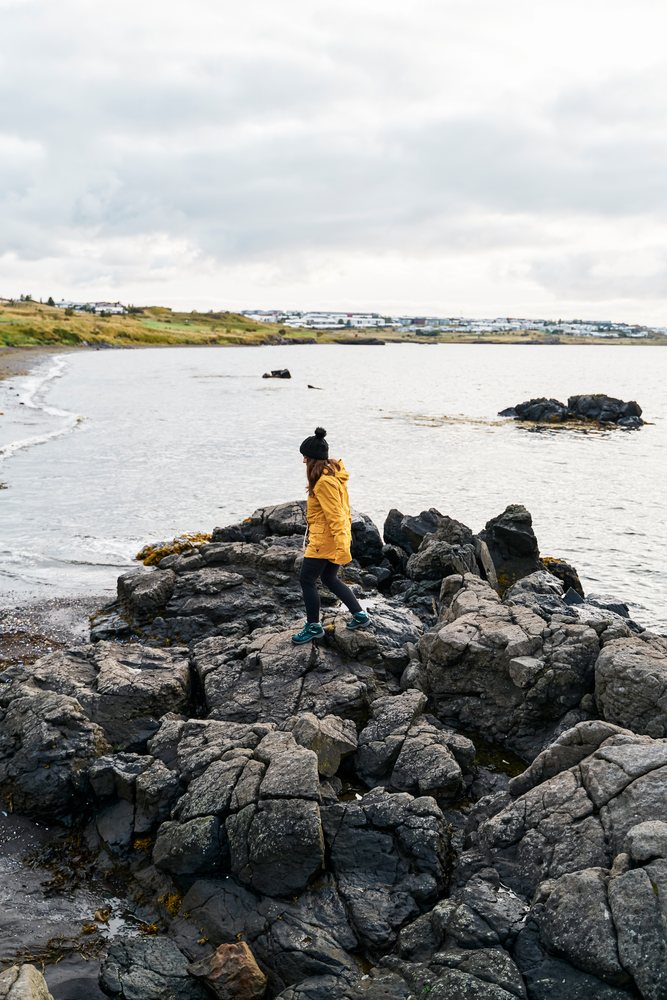 A white woman walks on rocky shore beside water
