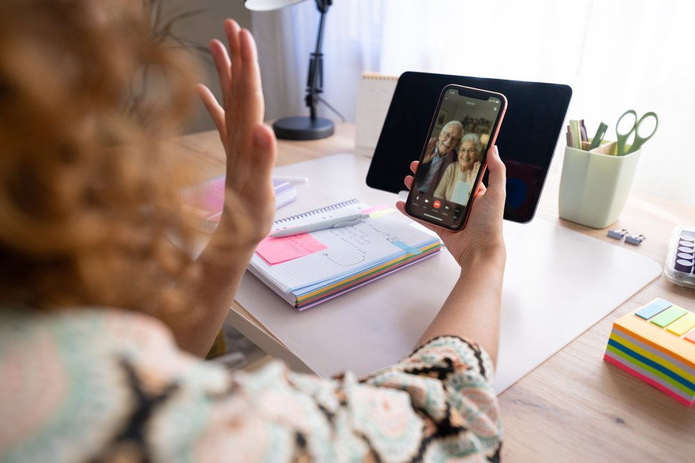 Woman with curly hair waving during a video call with an elderly couple at a desk in a Spanish home office, Spain.
