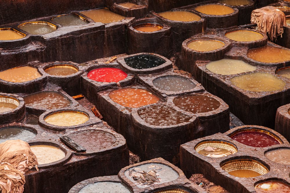 Multiple circular dye vats filled with colorful liquids at the outdoor Chouara tannery in rain, Landscape, Lifestyle, Fes, Fes-Mekners Administrative Regio, Morocco.