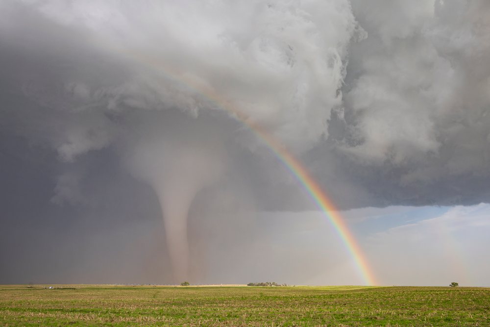 Visible Tornado funnel cloud touches the ground under dark storm clouds, with a Double Rainbow spanning the sky above a green grassy field, Dickens, Nebraska, USA.