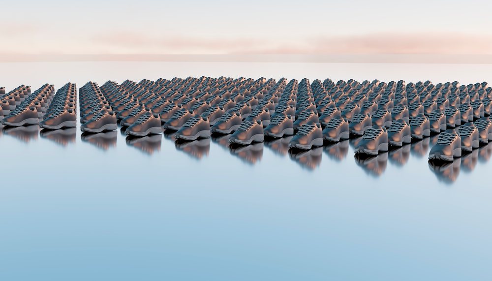 Pairs of grey shoes arranged in organized rows on a reflective surface creating a pattern effect.