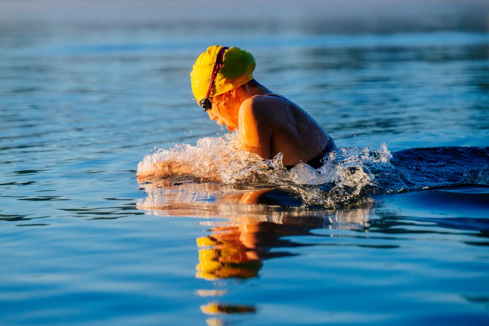 Adult swimmer wearing a swim cap and goggles performing breaststroke in open water at a lake, USA.