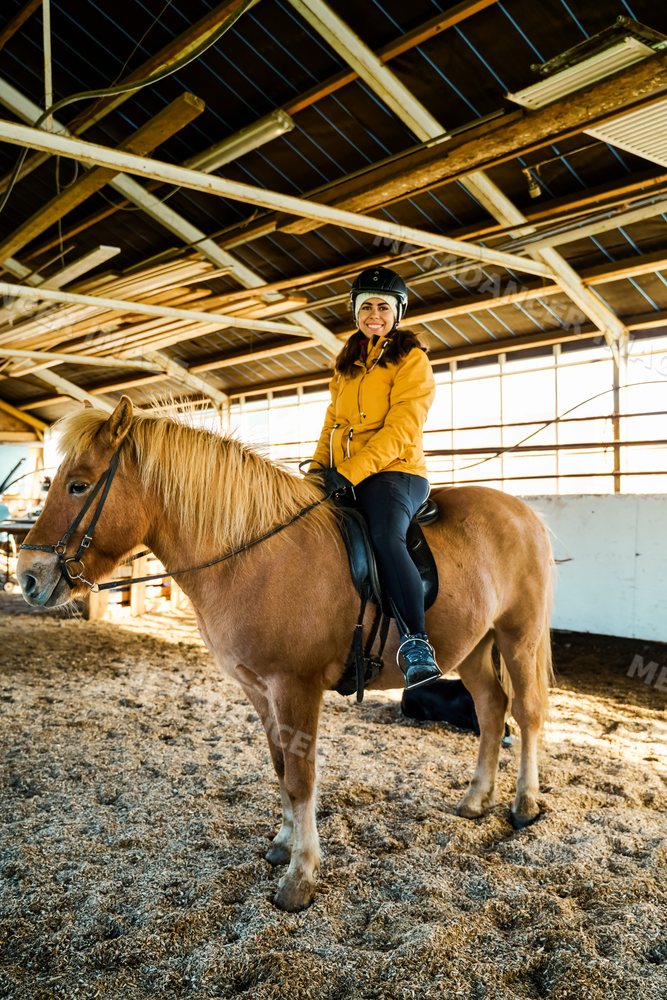 A white woman rides a brown horse inside a stable in Iceland