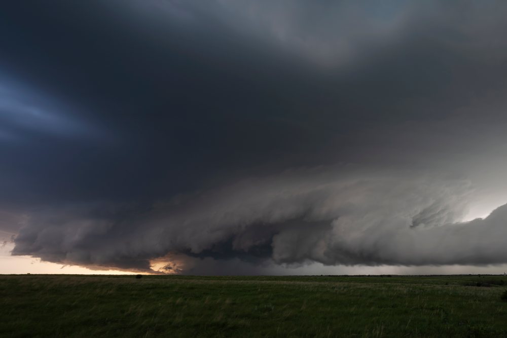 Supercell thunderstorm displaying a Huge Inflow Tail beneath dark storm clouds over green grassy fields, Storm Chasing, Weather, Environmental Issues, Herrington, Kansas, USA.