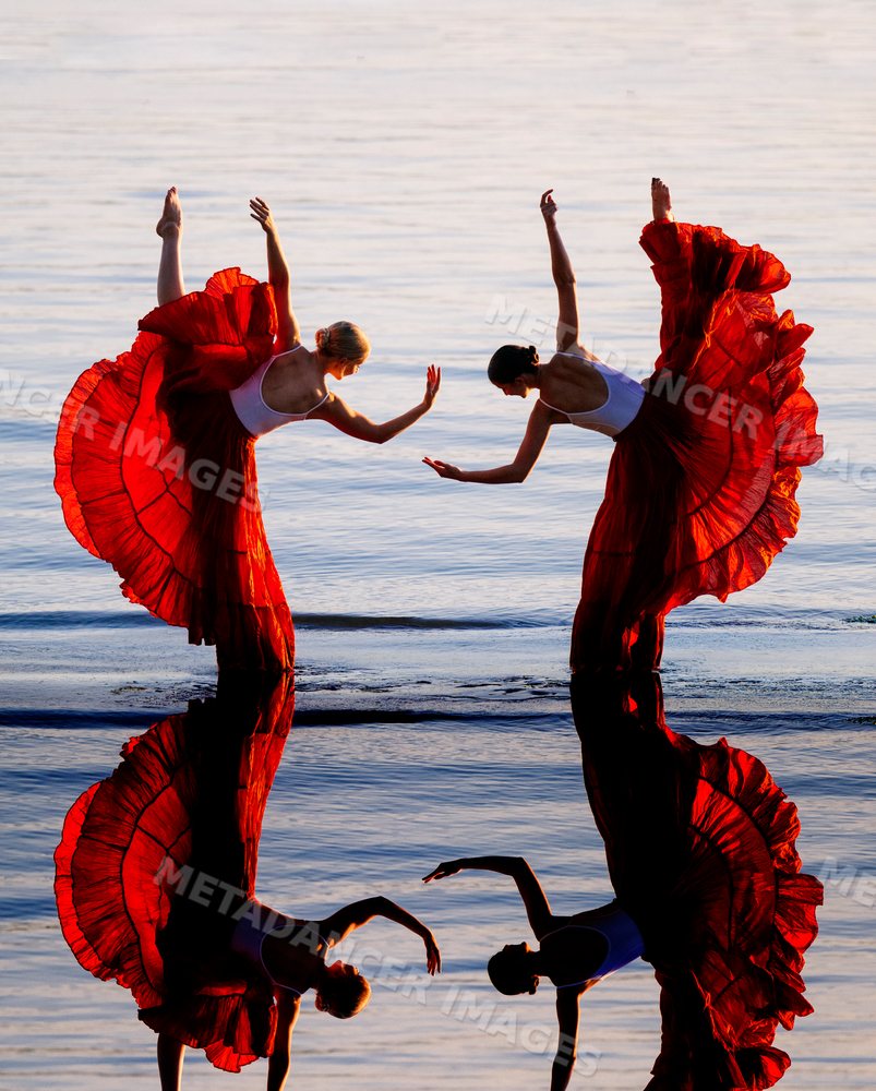 Two white women practicing partner yoga acrobatics with red skirts