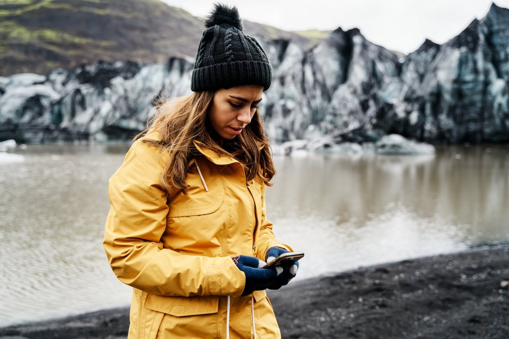 A white woman uses her smartphone near a glacier lake