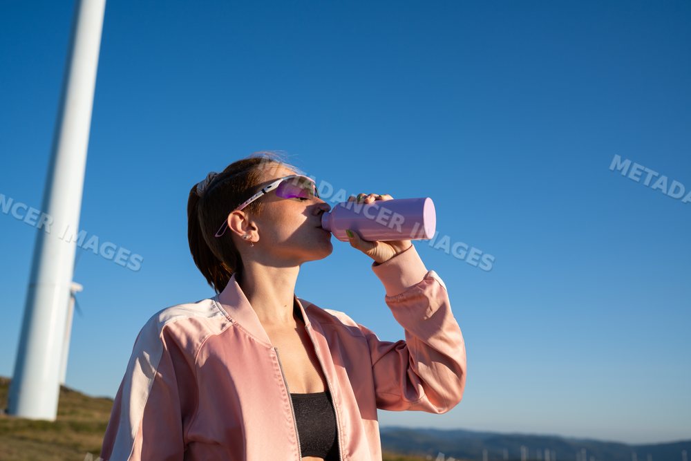 White Woman drinking water outdoors near wind turbines in Galicia
