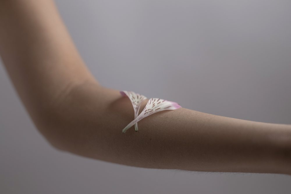 Flower petals delicately placed on a smooth human arm against a neutral background under soft natural light, Art, portrait, emotional.