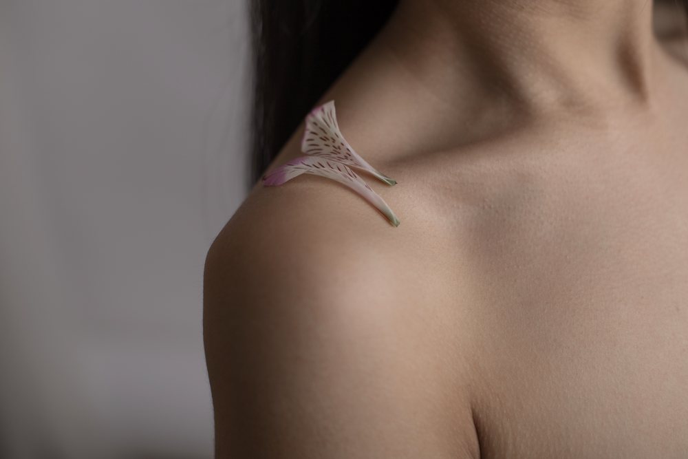 Close-up of a human shoulder with delicate flower petals resting on smooth skin under soft natural lighting, Art, portrait, emotional.