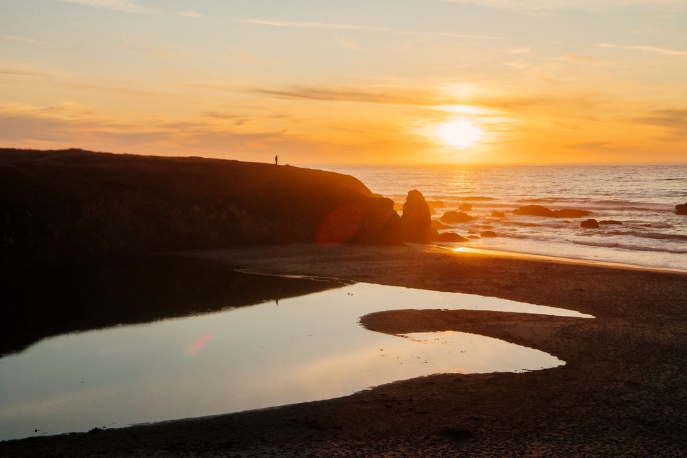 Sunset over rocky beach cliffs and calm ocean shore reflecting on wet sand at Oregon-California coast, northern, USA.