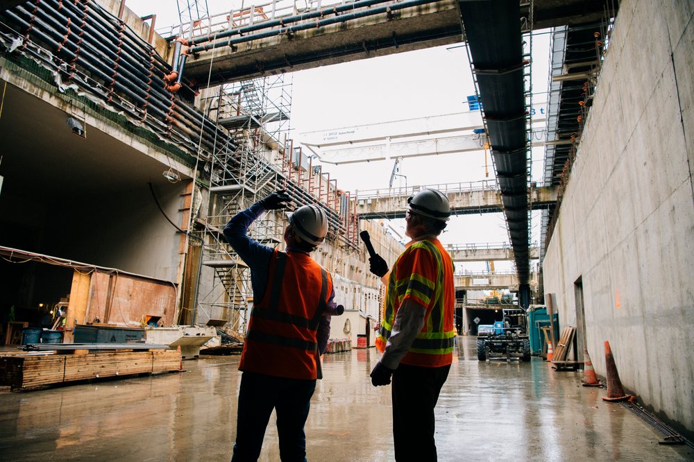 Two construction workers in safety gear discussing progress inside a large tunnel construction site, Bertha, drilling, USA.