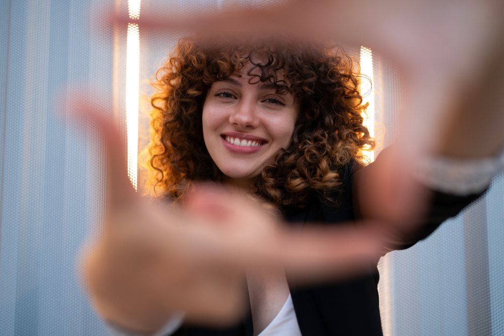 Smiling woman with curly hair reaches her hands toward the camera outdoors, young business, Madrid.