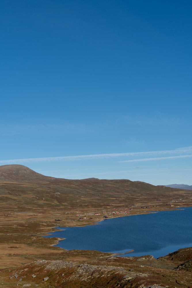 Calm lake with hills and scattered small houses under a clear blue sky, Norway.