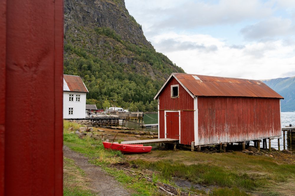 Red wooden boathouse with dock and red rowboat on shore of Luster, coastal town, village, Fjord, Norway.