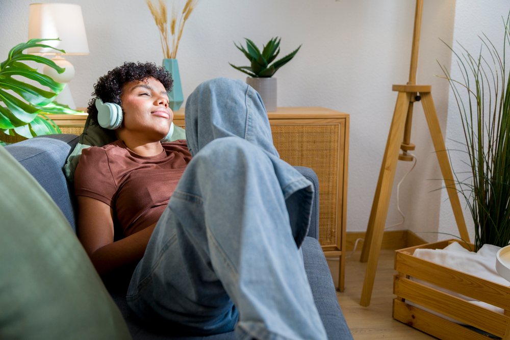 Young woman reclining on a sofa in a living room while listening to music with headphones at home.