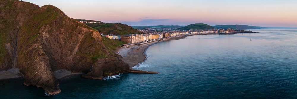Coastal town of Aberystwyth at Dusk showing cliffs, beach, calm sea, and hills, Landscape, Aberystwth, Ceredigion, Wales.