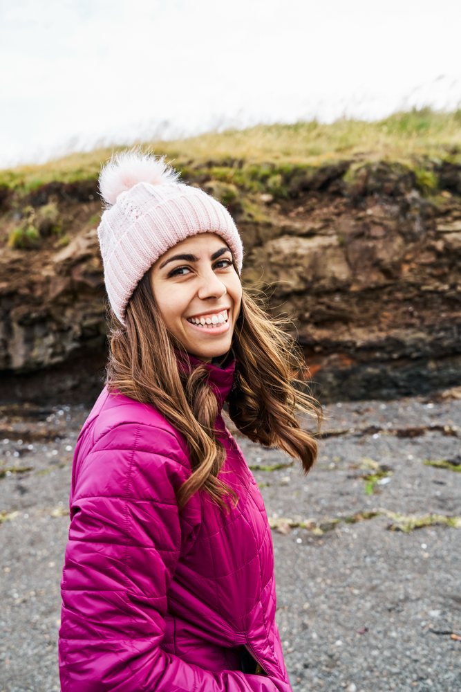 A smiling white woman wearing a pink winter hat and jacket outdoors