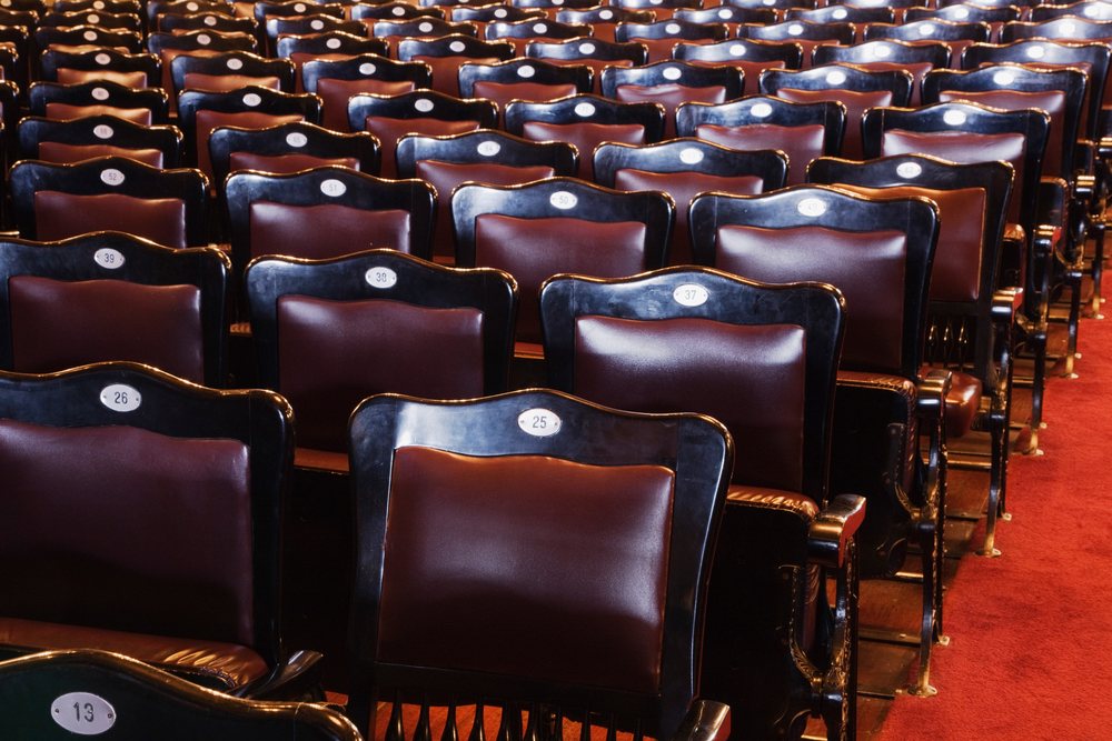 Rows of empty numbered theater seats with leather backs and wooden armrests on red carpet, San Jose, Costa Rica.