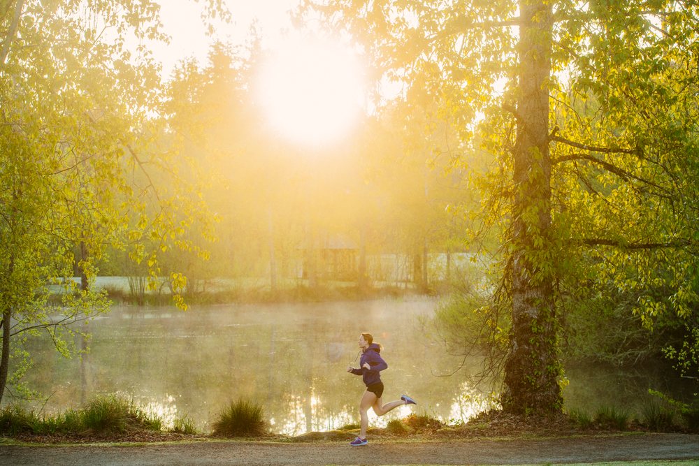 Runner jogging along a trail beside a lake in a misty park morning, Bainbridge Island, Wa, USA.