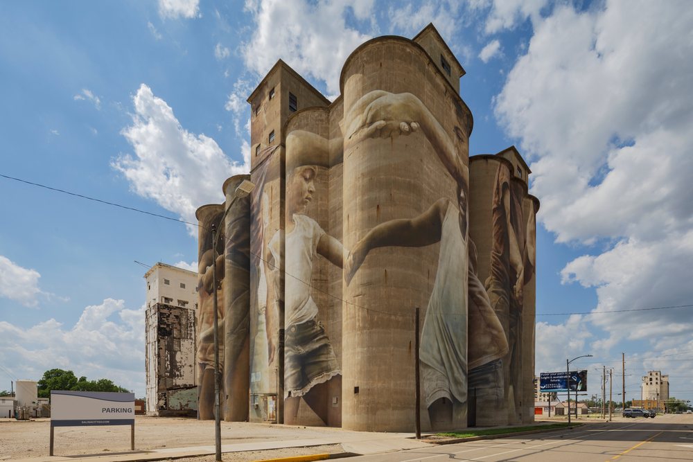 Large Grain Silo, features a mural of children holding hands under a partly cloudy sky in an urban setting, Storm Chasing, Weather, Environmental Issues, Salina, Kansas, USA.
