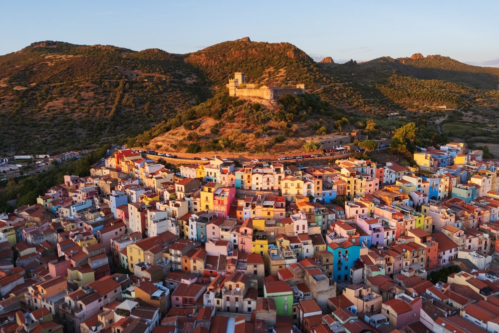 Sunset view over Bosa, showing colorful houses clustered in the old town with a castle atop a hill, Travel Images, Sardinia, Italy.