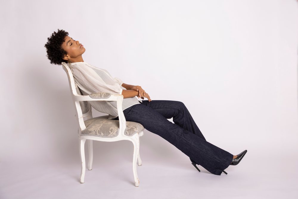 Woman relaxing while sitting on a vintage chair in a minimalist white studio setting, fashion, young culture.