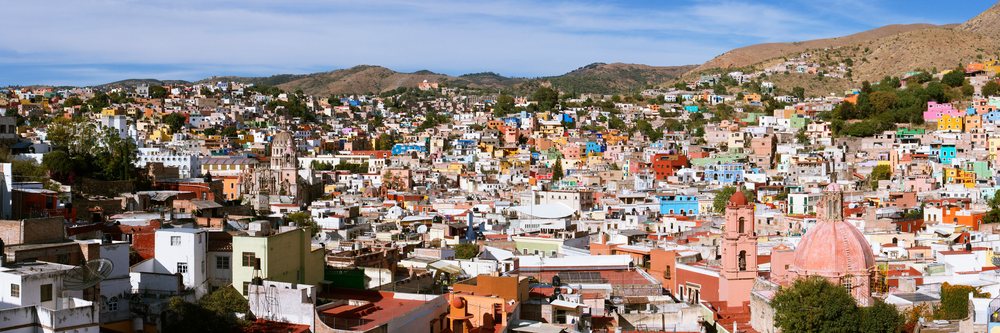 Panoramic view of colorful buildings and hills, Mexico under a clear sky.