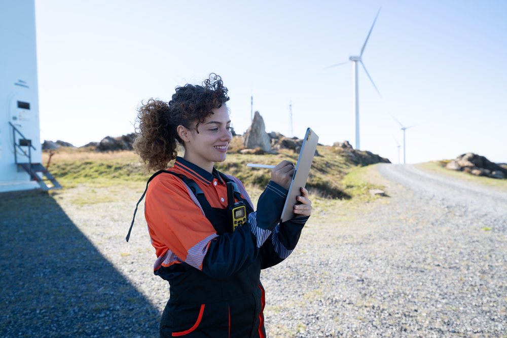 Woman engineer holding and using a tablet with stylus at a wind farm, with wind turbines in the background, sustainability, renewable energy, Galicia, Spain.