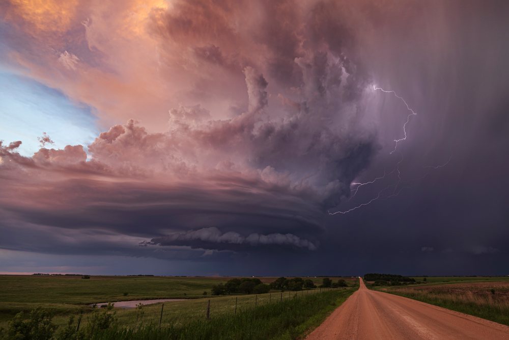 Supercell thunderstorm with Lightning striking over rural dirt road and open grassy fields at Sunset, Storm Chasing, Weather, Environmental, Jansen, Nebraska, USA.