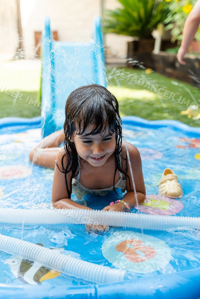 A young white girl enjoys playing in an inflatable pool on a sunny day