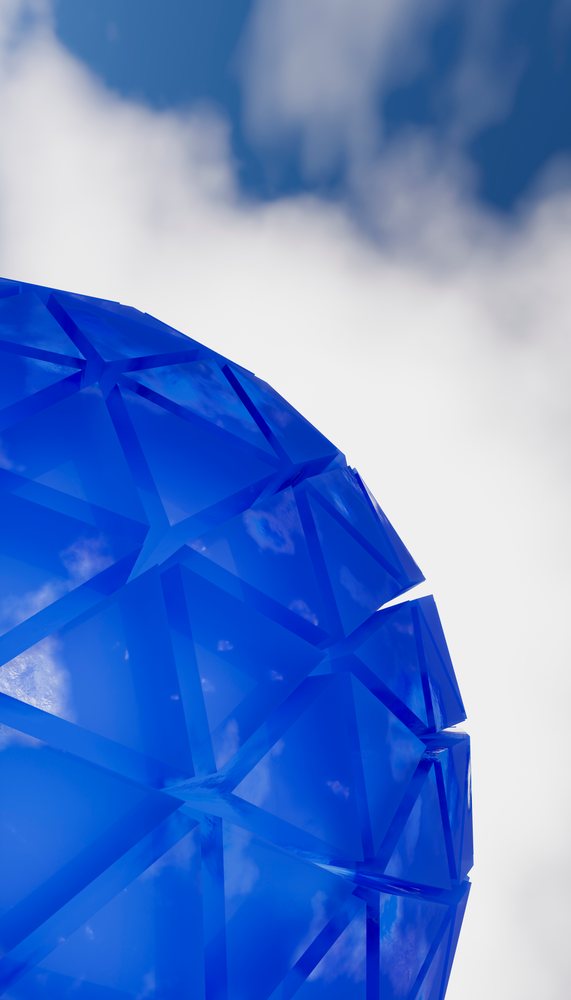 Blue geometric dome made of triangular glass panels reflecting the sky and clouds, showing modern architectural design outdoors.
