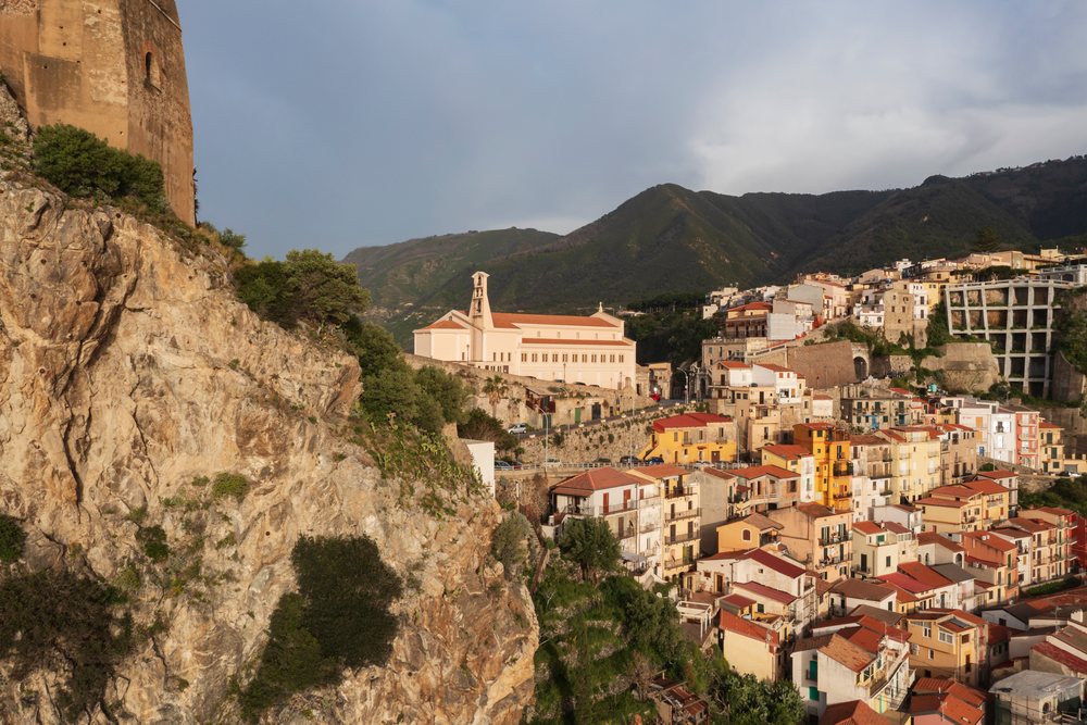 Scilla town, Italy featuring Castello Ruffo castle and Chiesa Maria Santissima Immacolata church with a mountainous background, Calabria.