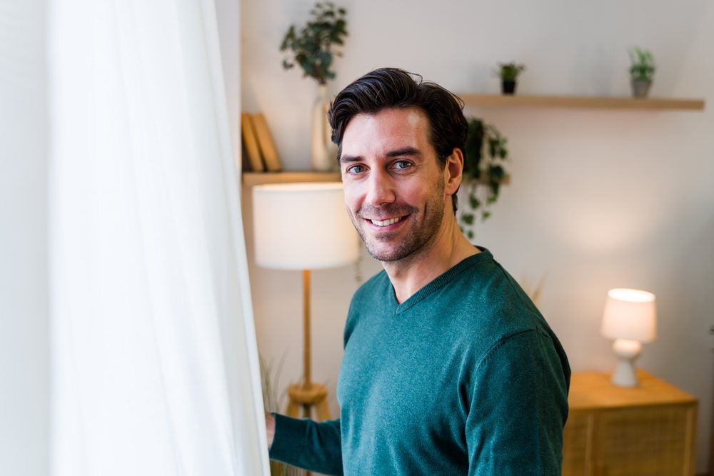 Smiling man stands indoors near a window, Spain.