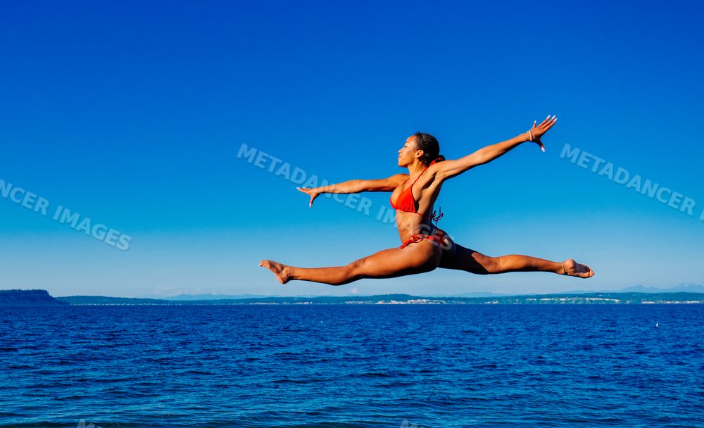 A woman jumps in a red bikini over the ocean on a clear sunny day