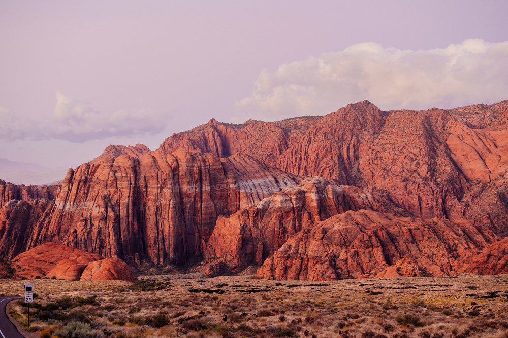 Red cliffs and rugged rock formations rise among arid desert vegetation along a road with a speed limit sign, Snow Canyon, red Cliffs Desert, Utah, USA.