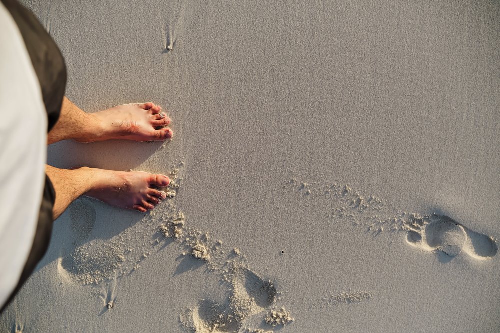 Person standing barefoot on soft sand with footprints on a beach