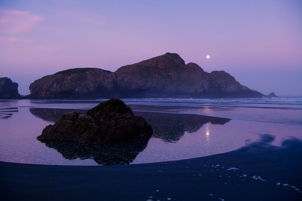 Rock formations and full moon reflected in tide pools on a coastal beach at twilight, Meyers Creek, Oregon, USA.