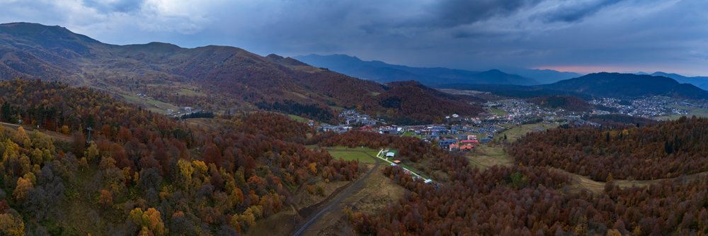 Panoramic view of Bakuriani mountain town amid autumn forest and hills in Georgia under a cloudy sky.