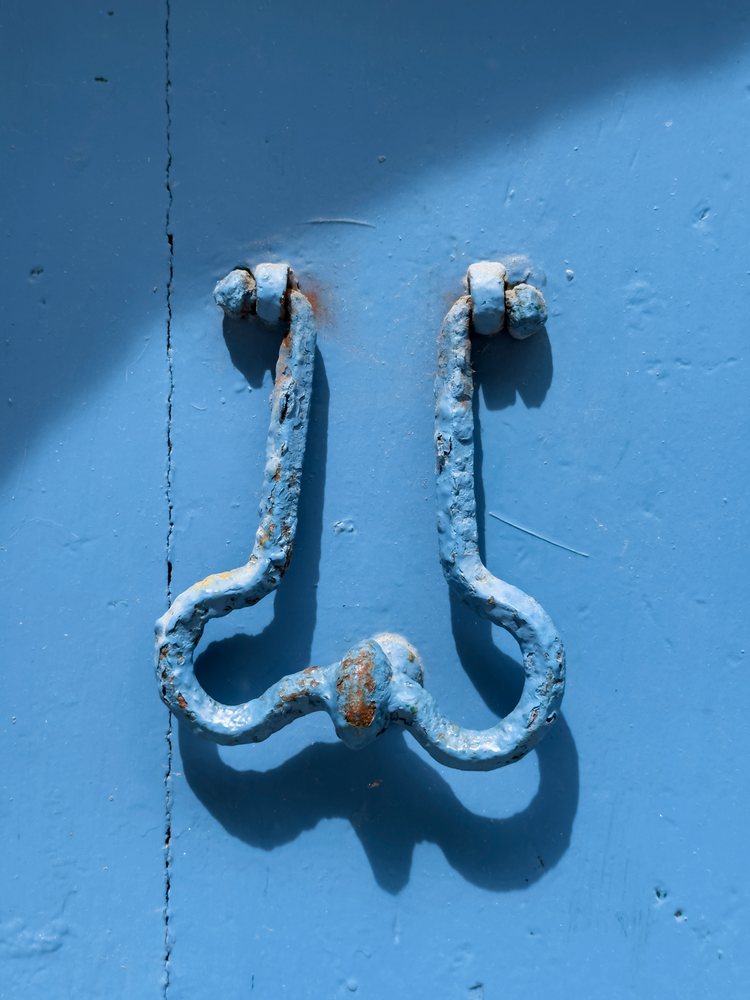 Weathered metal door knocker decorates a blue exterior door, Scilla, Calabria, Italy.