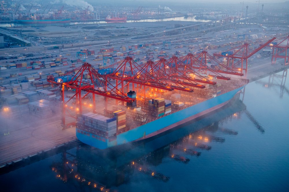 Container ship loading cargo at container cranes in the Port of Long Beach during early morning mist, CA, USA.